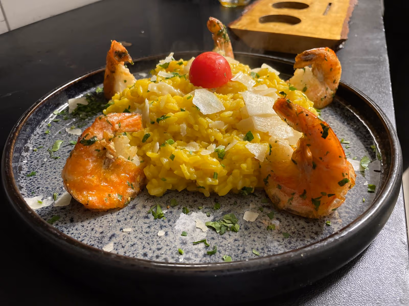 Reisgericht mit Garnelen und Sauce, angerichtet auf schwarzem Teller.