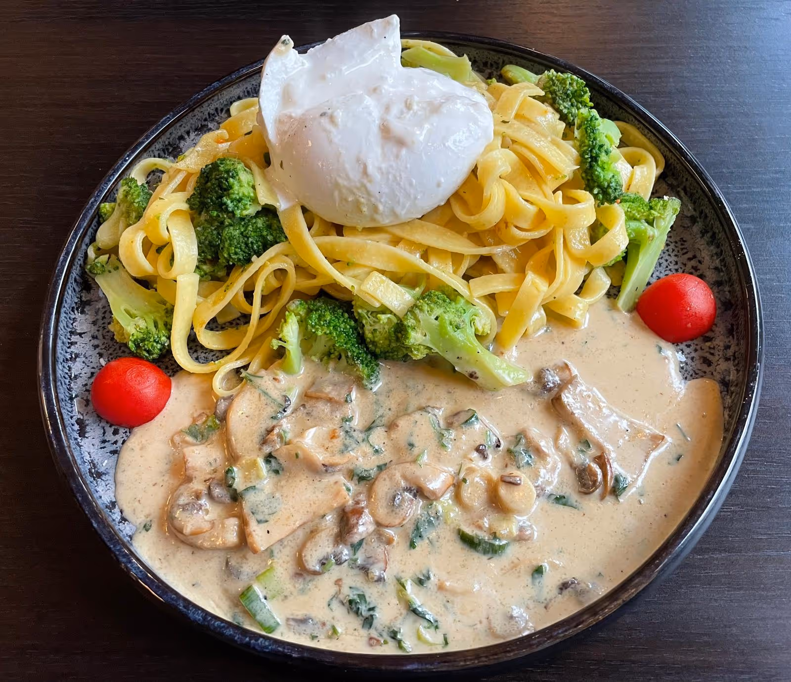 Pasta mit Spinat, Tomaten und Parmesan auf schwarzem Teller.